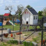 A wooden backyard chicken coop with a chicken standing near the entrance